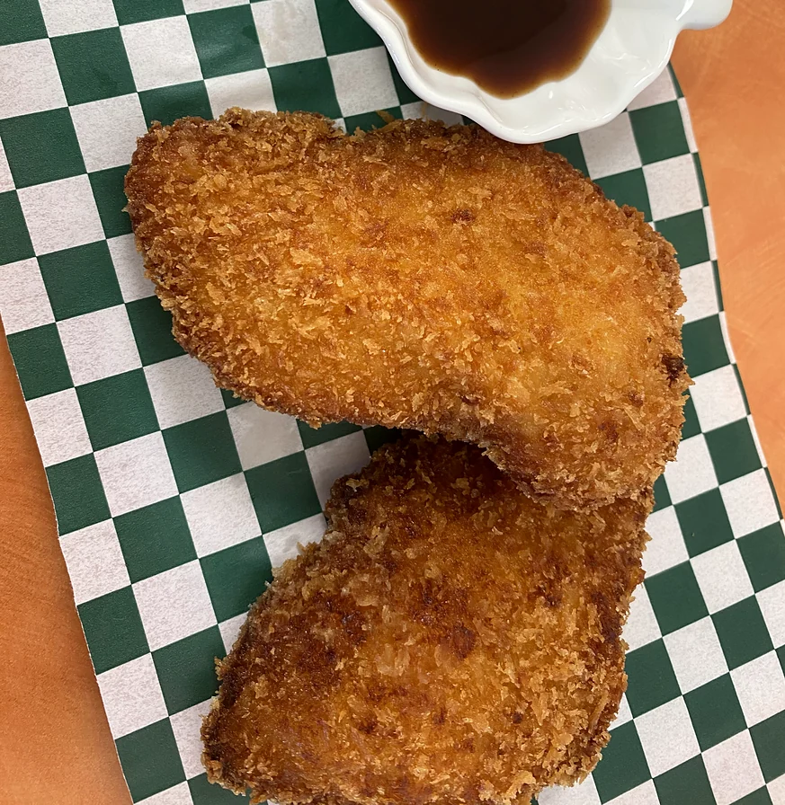 Two pieces of panko-breaded chicken katsu on checkered paper with dipping sauce at Hana Sushi, Winnipeg